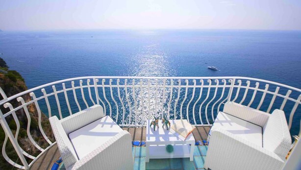 Een balkon met witte rieten meubels en een helder uitzicht op zee.
