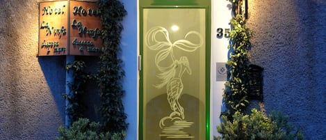 A hotel entrance with a green door, a sign with the name "La Ninka," and two potted plants on either side.