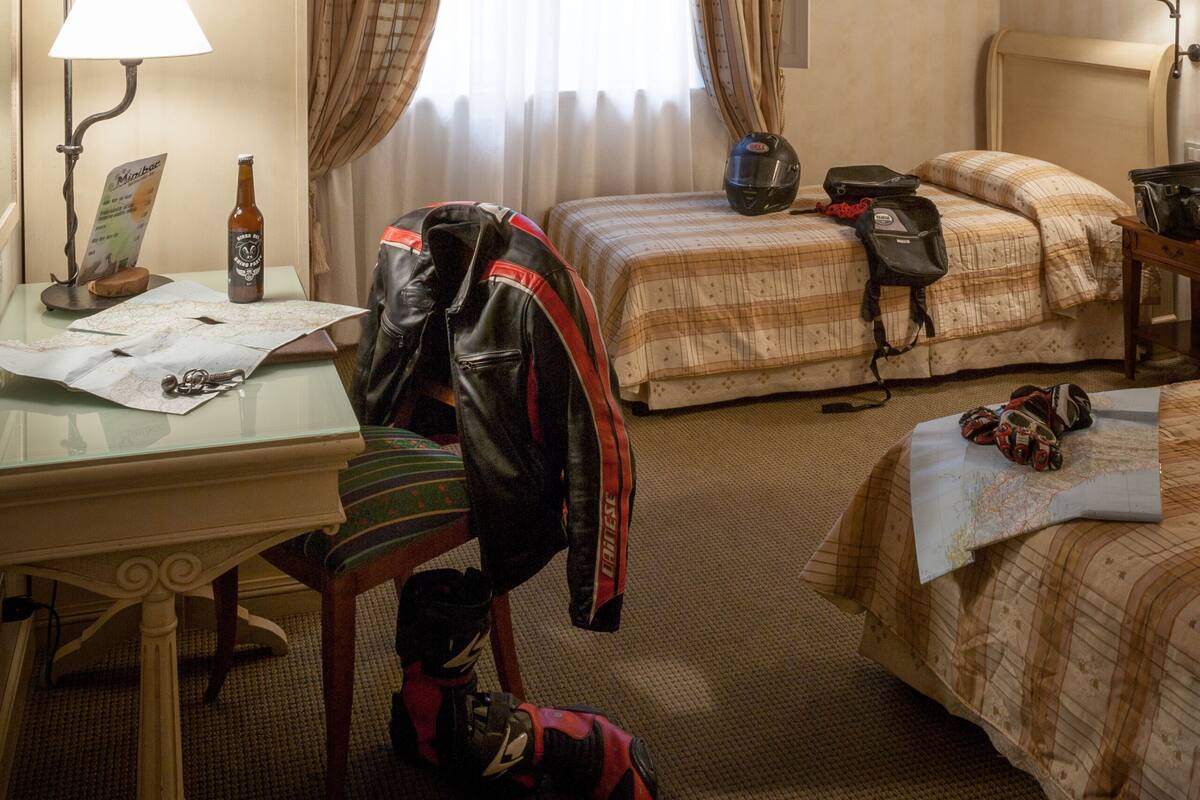 Une chambre d’hôtel avec un plafond en bois, deux lits avec une literie à carreaux, un bureau avec une lampe et une fenêtre avec des rideaux.