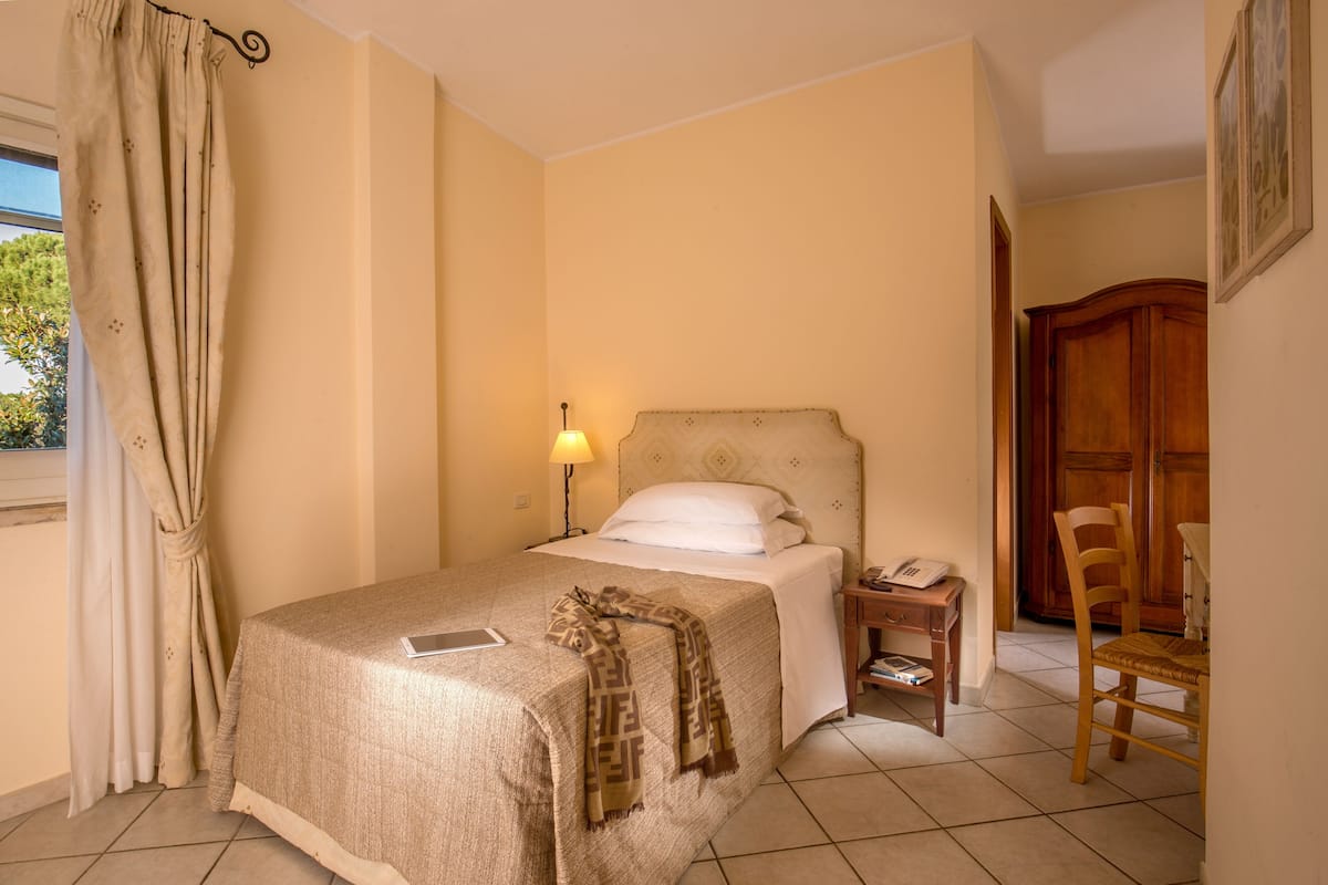 Une chambre d’hôtel comprenant un lit, une table de chevet, une lampe, une chaise et une armoire en bois.