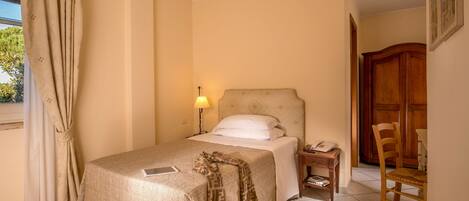 Une chambre d’hôtel comprenant un lit, une table de chevet, une lampe, une chaise et une armoire en bois.