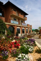 Um hotel com fachada de tijolos, várias varandas e um jardim com flores coloridas.