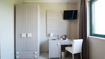 Une chambre d’hôtel équipée d’un bureau, d’une chaise, d’une télévision, d’une armoire et d’une fenêtre avec des rideaux.