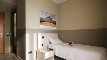 Camera d'albergo con un letto, un comodino con una lampada, un telefono e un tavolino con un laptop. Sulla parete sopra il letto è appeso un poster.