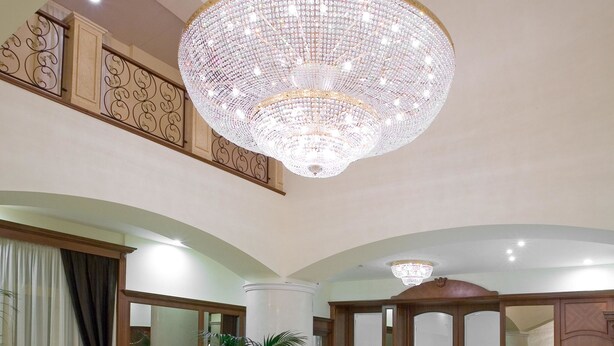 Um lobby amplo com um grande candelabro, uma mesa de recepção e uma área de estar com um tapete estampado com padrão de estrelas.