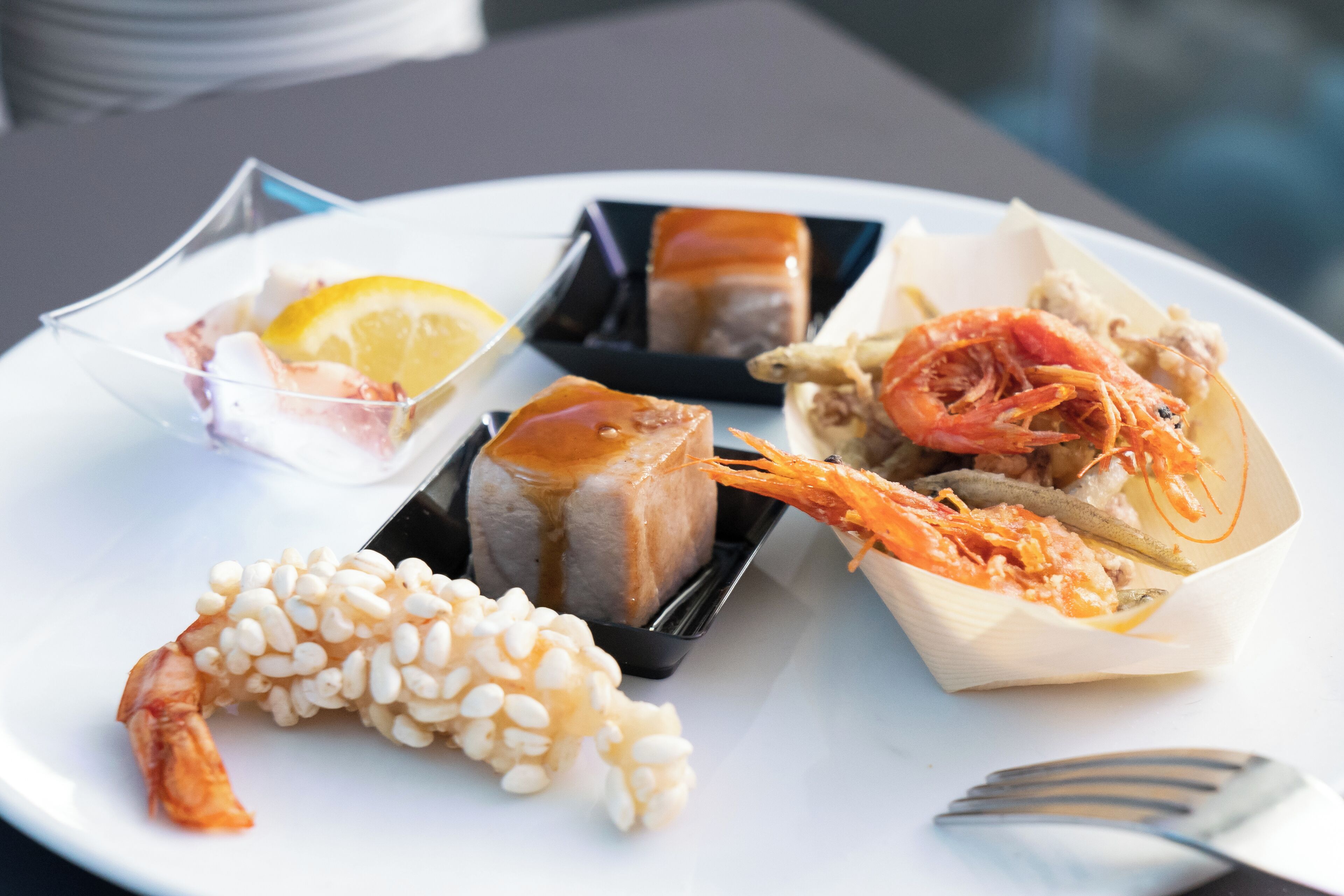 A plate with various seafood dishes, including shrimp and fish, arranged on a white plate.