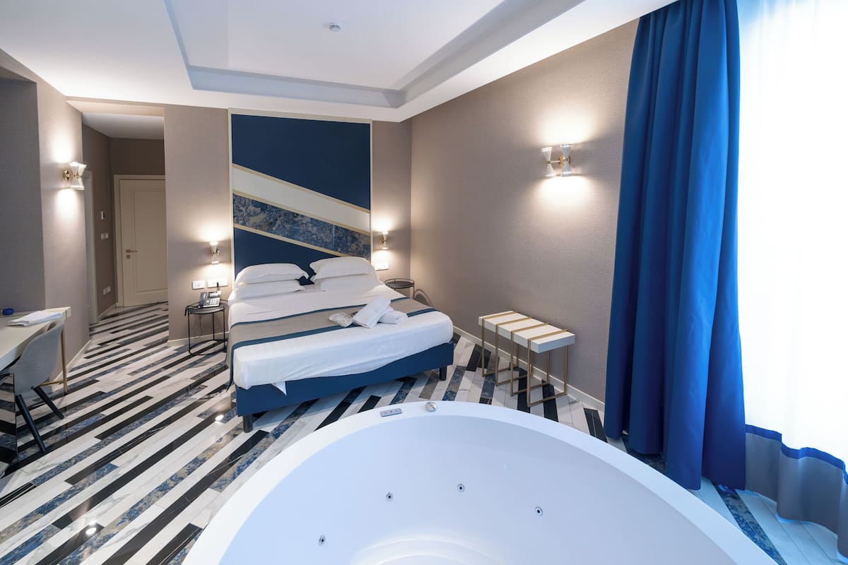A modern hotel room with a large bed, a separate bathroom, a desk, and a view of the cityscape.
