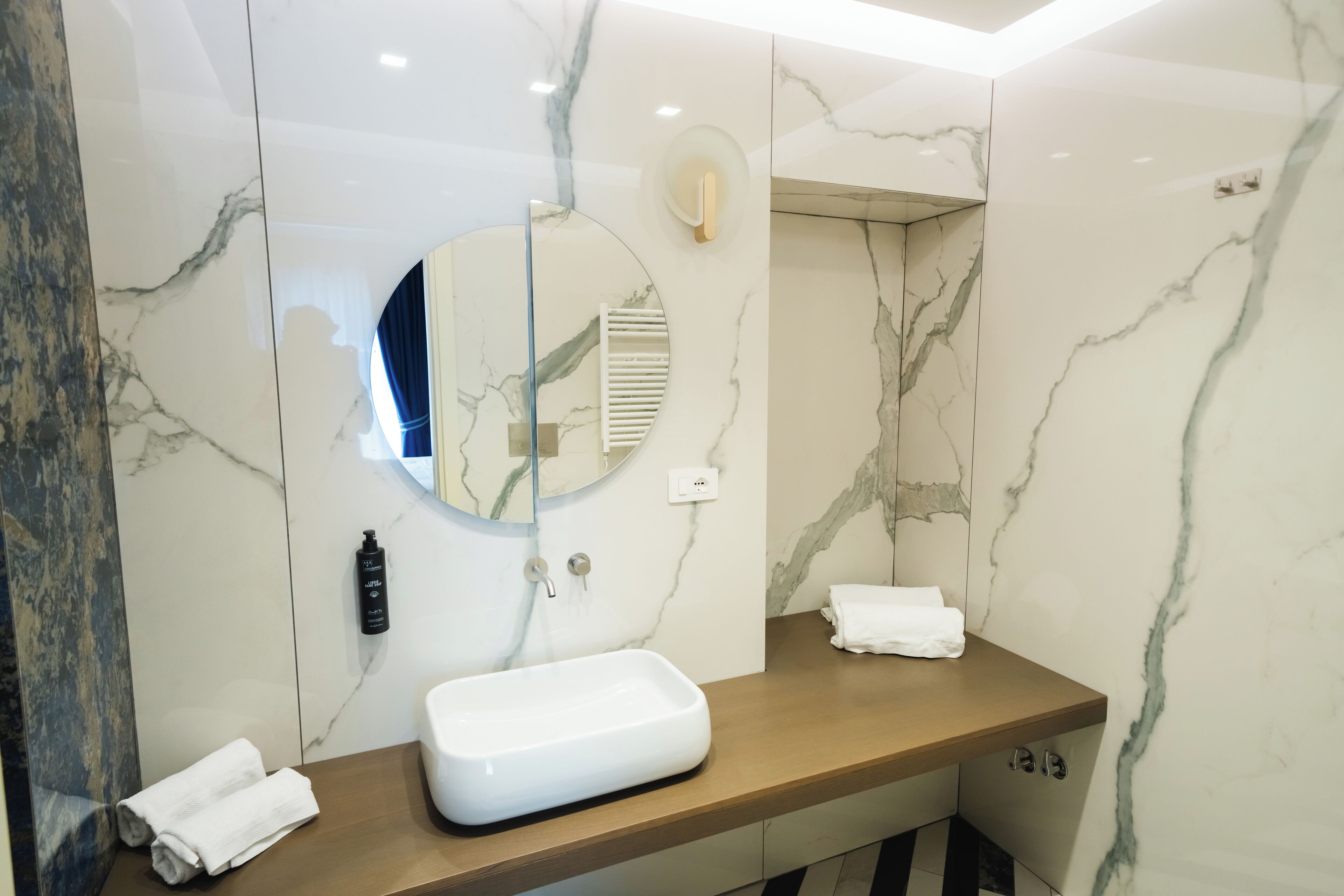 Une salle de bain moderne avec un meuble-lavabo en marbre, un miroir rond et un porte-serviettes.