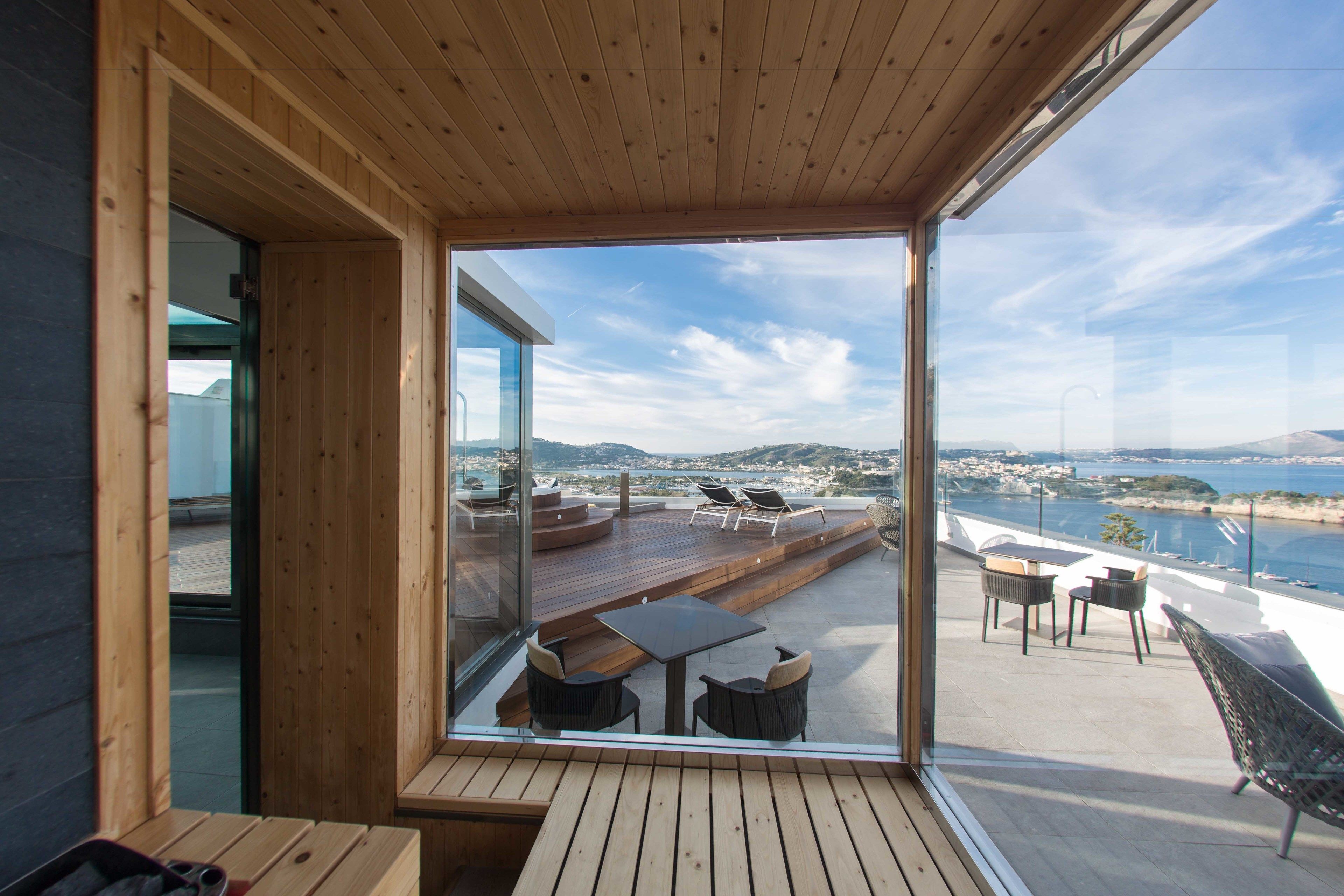Un interior moderno con una terraza de madera, paredes de vidrio y vistas a un paisaje costero.