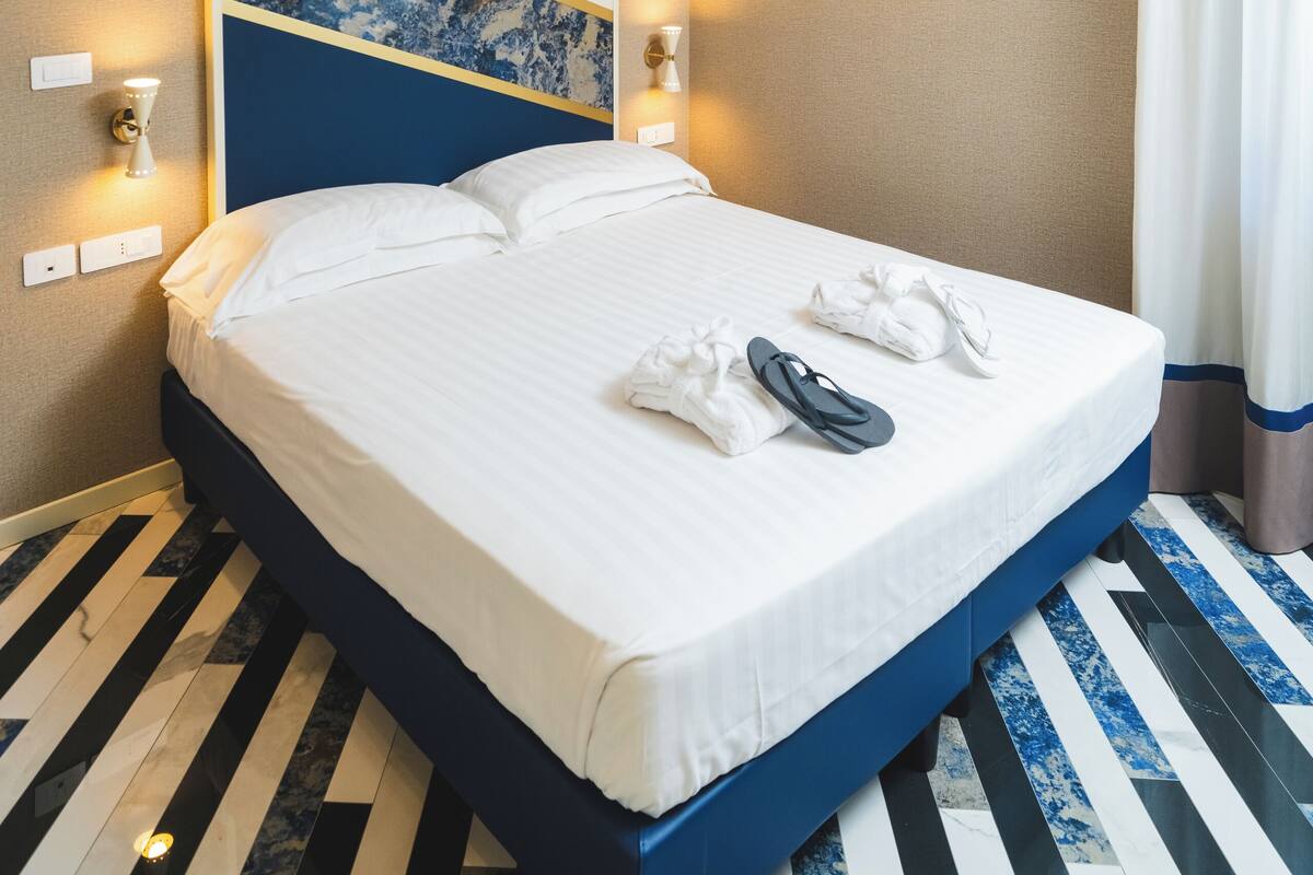 A hotel room with a large bed, a blue accent wall, and a marble-patterned floor.
