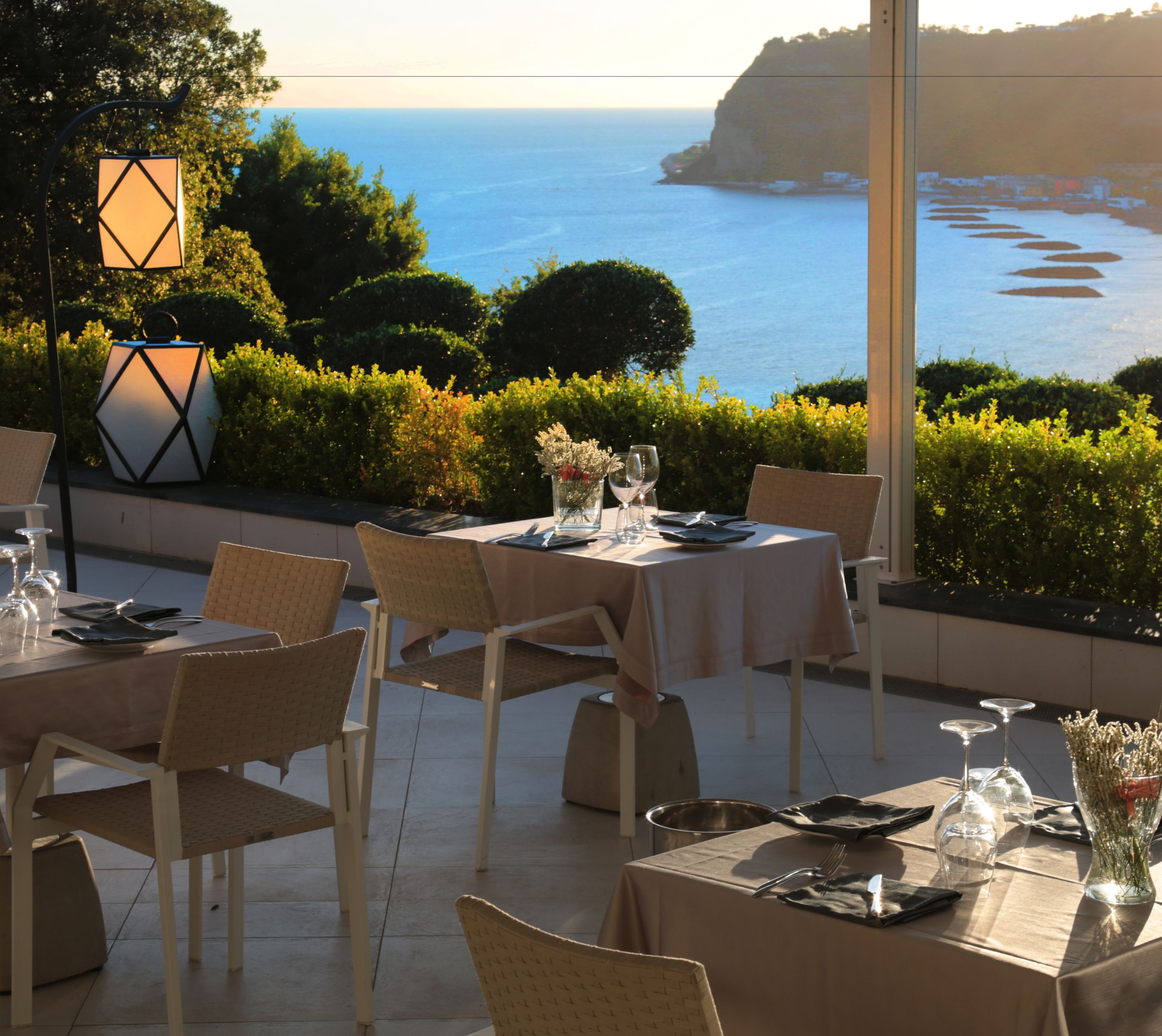 Un área de comedor al aire libre con mesas dispuestas para dos, con vistas a la costa.