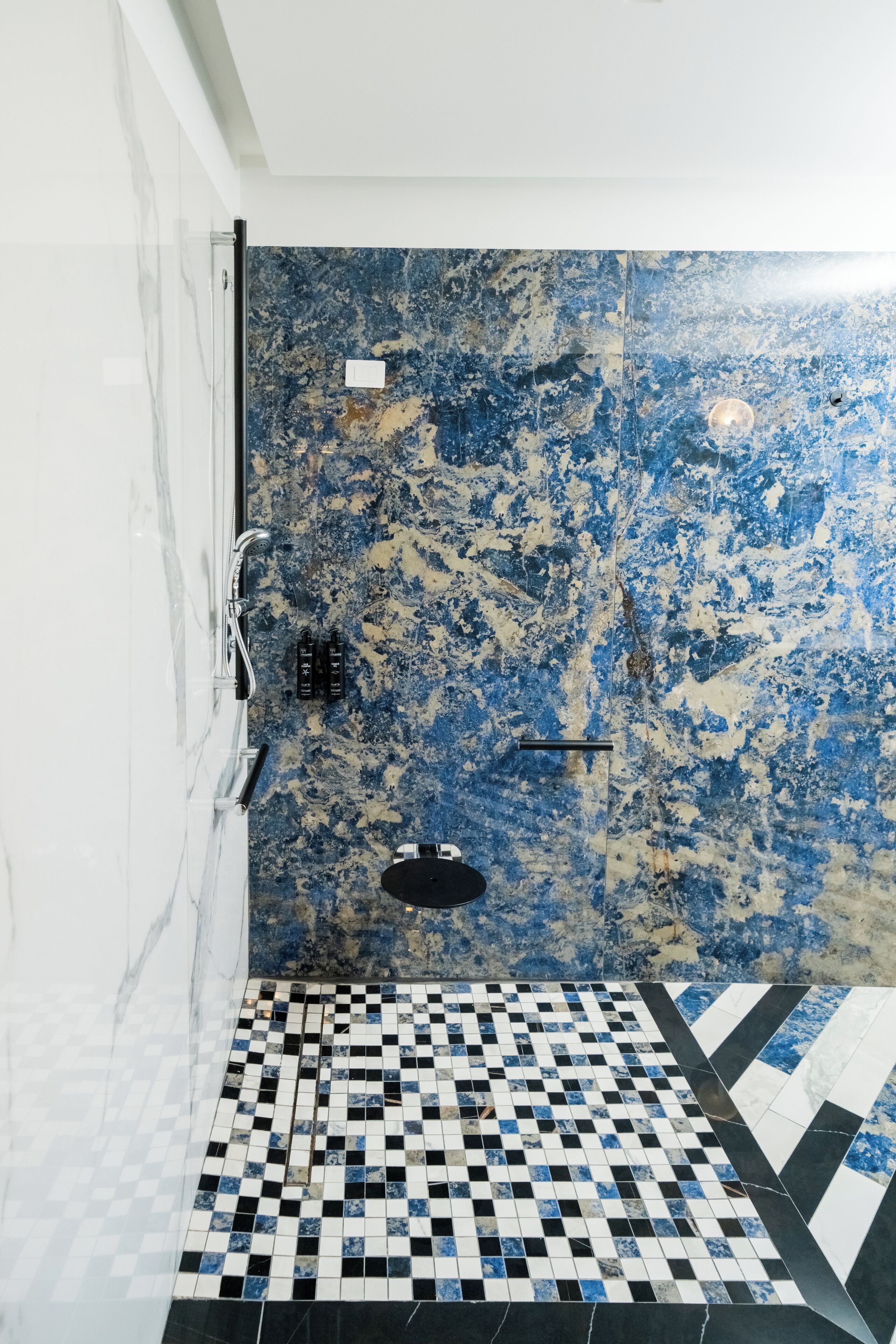 A bathroom with a checkered floor, a shower with a blue and white marble wall, and a white tiled wall.