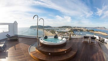 Relax on the deck overlooking the scenic coastal landscape, featuring a hot tub and comfortable lounge seating.