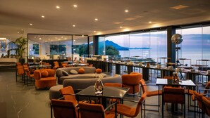 Een modern interieur met zithoeken, een bar en grote ramen met uitzicht op zee en bergen.