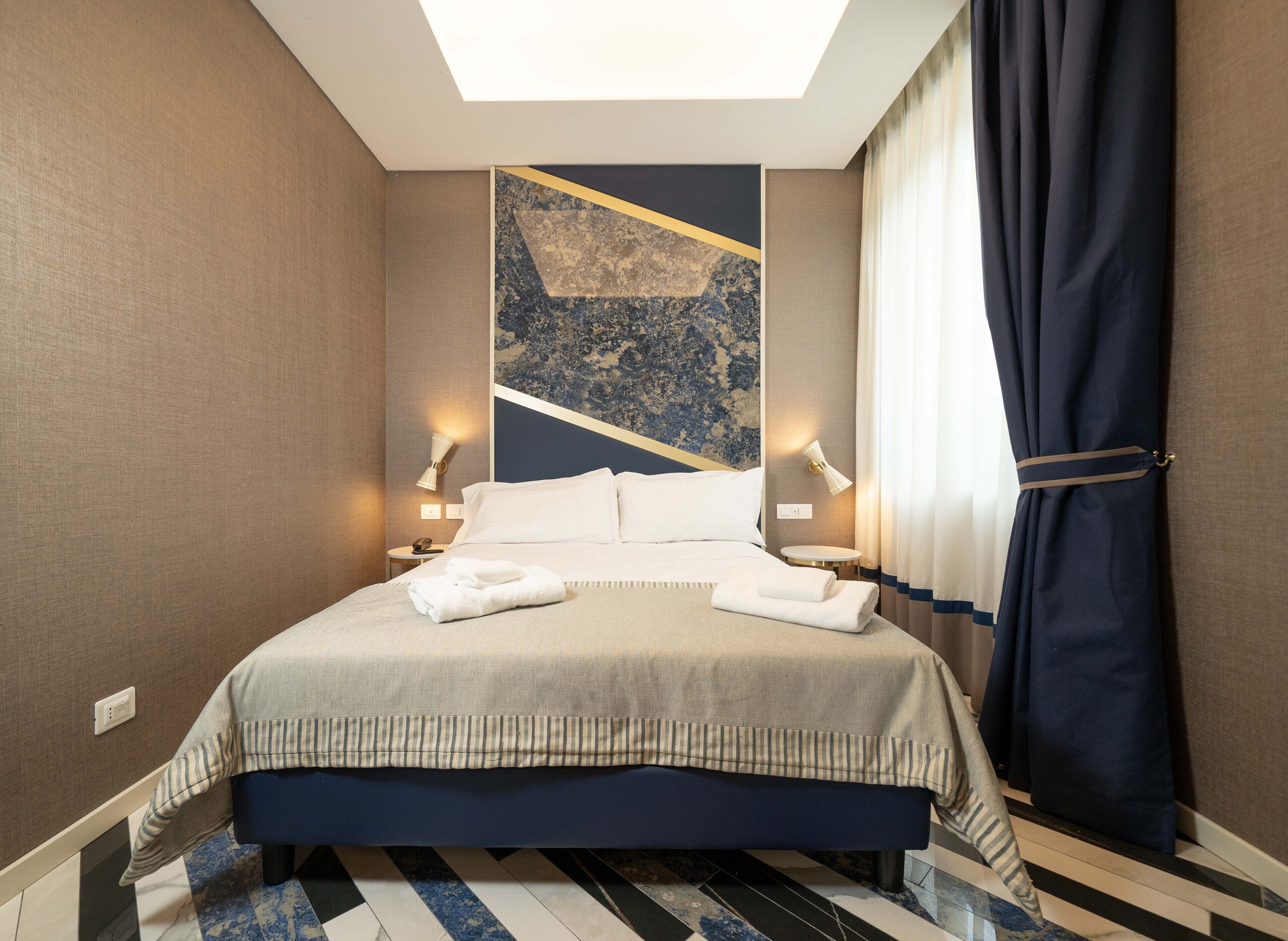 Ein Hotelzimmer mit einem Bett, zwei Nachttischlampen, einem Telefon und einem Fenster mit Vorhängen.