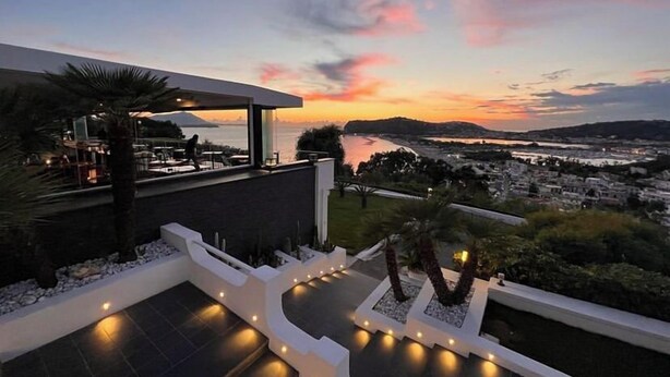 Een modern terras buiten met uitzicht op een waterpartij en een stadsbeeld bij zonsondergang.