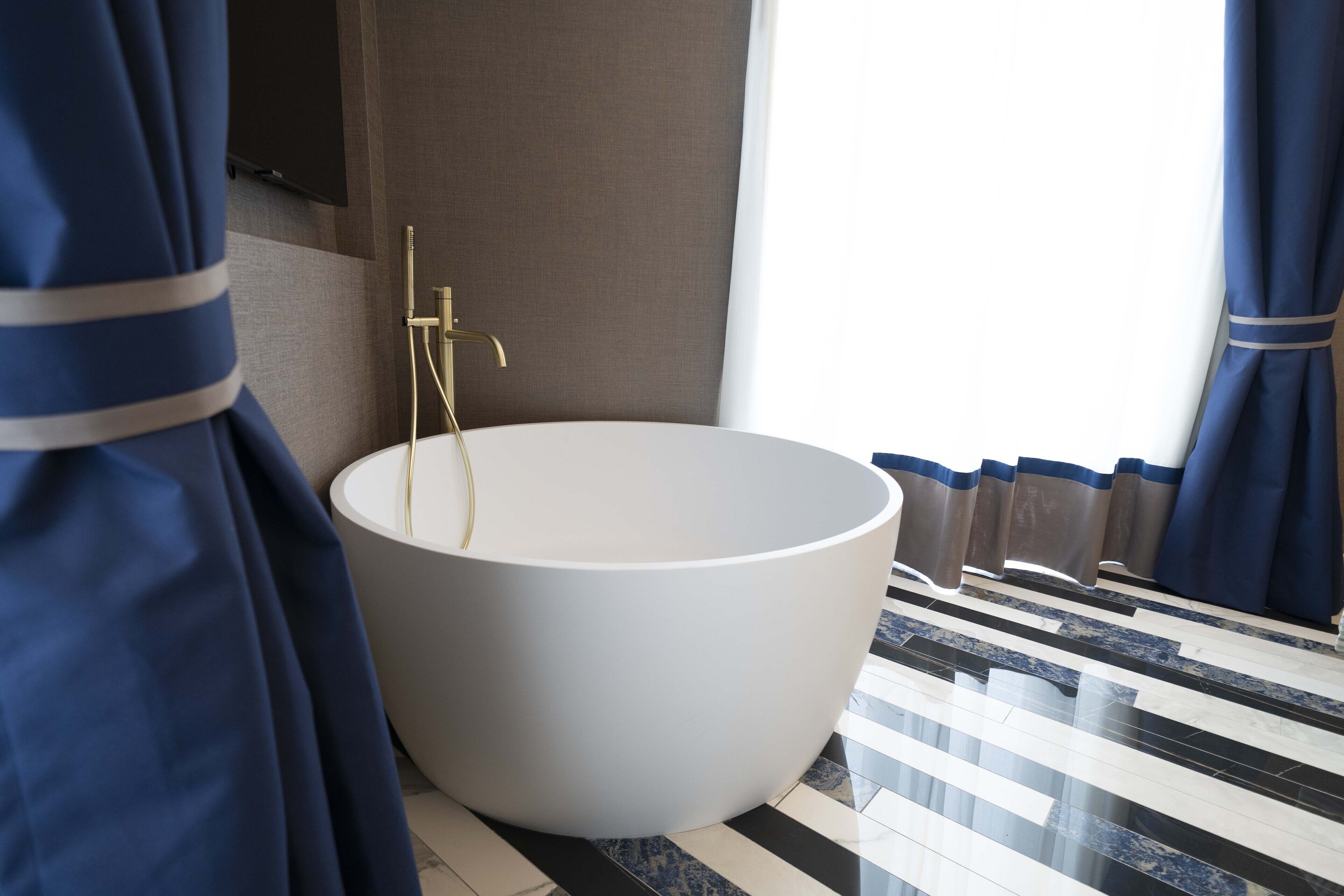 Un baño moderno con una bañera independiente grande, un grifo dorado y un piso a rayas.