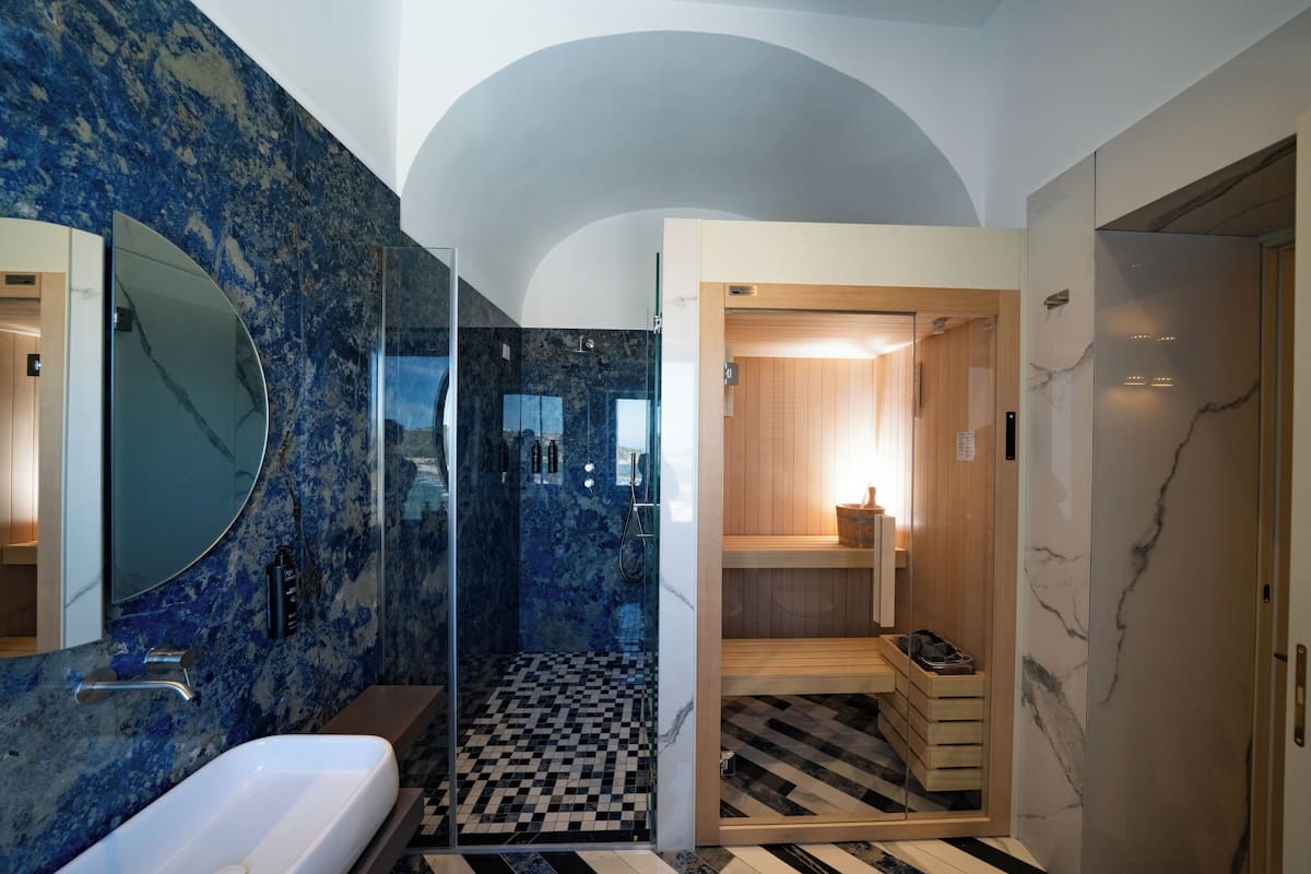 A modern bathroom with a glass-enclosed shower, a marble-tiled wall, and a checkered floor.