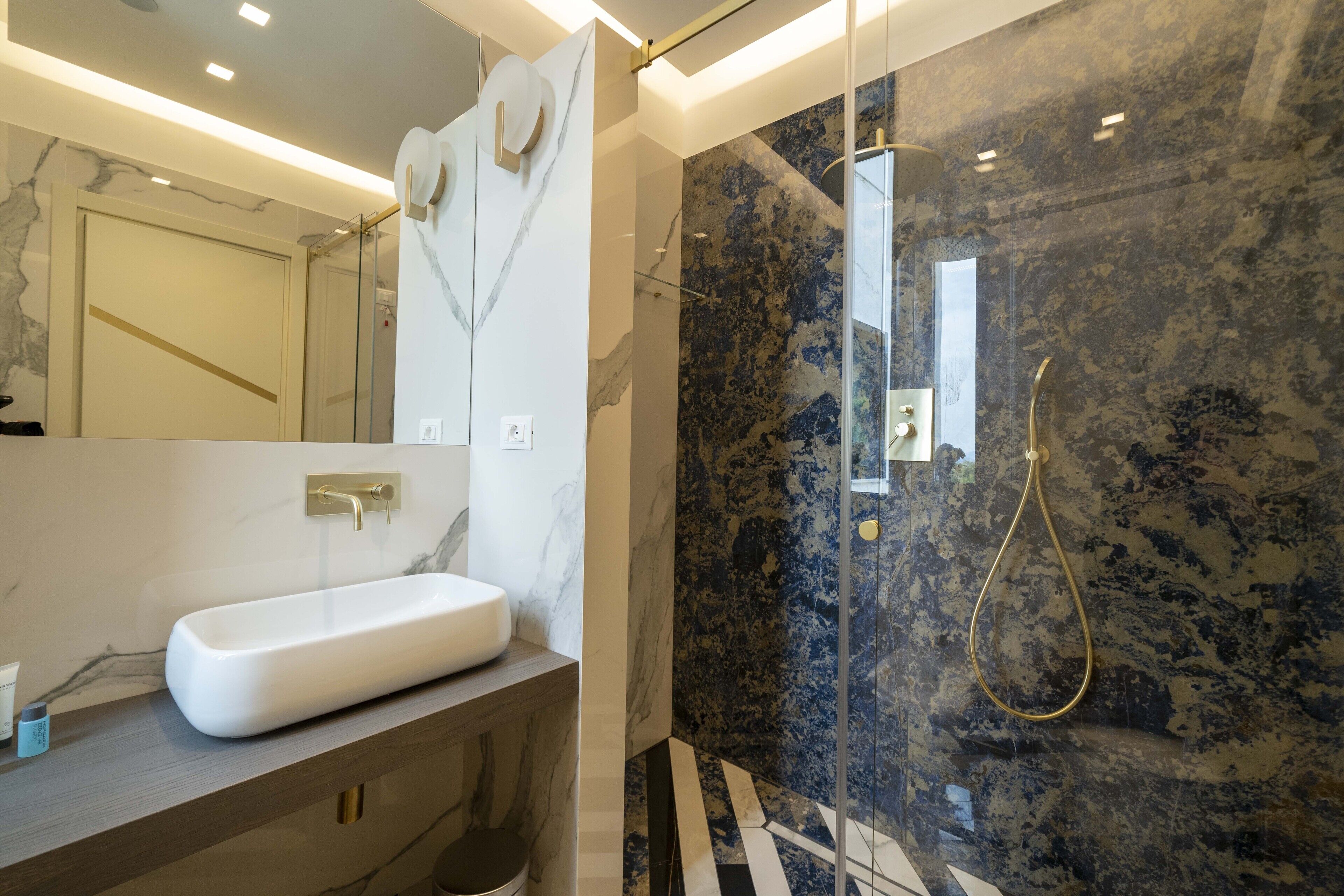 A modern bathroom with a marble sink, a glass-enclosed shower, and a marble-tiled wall.