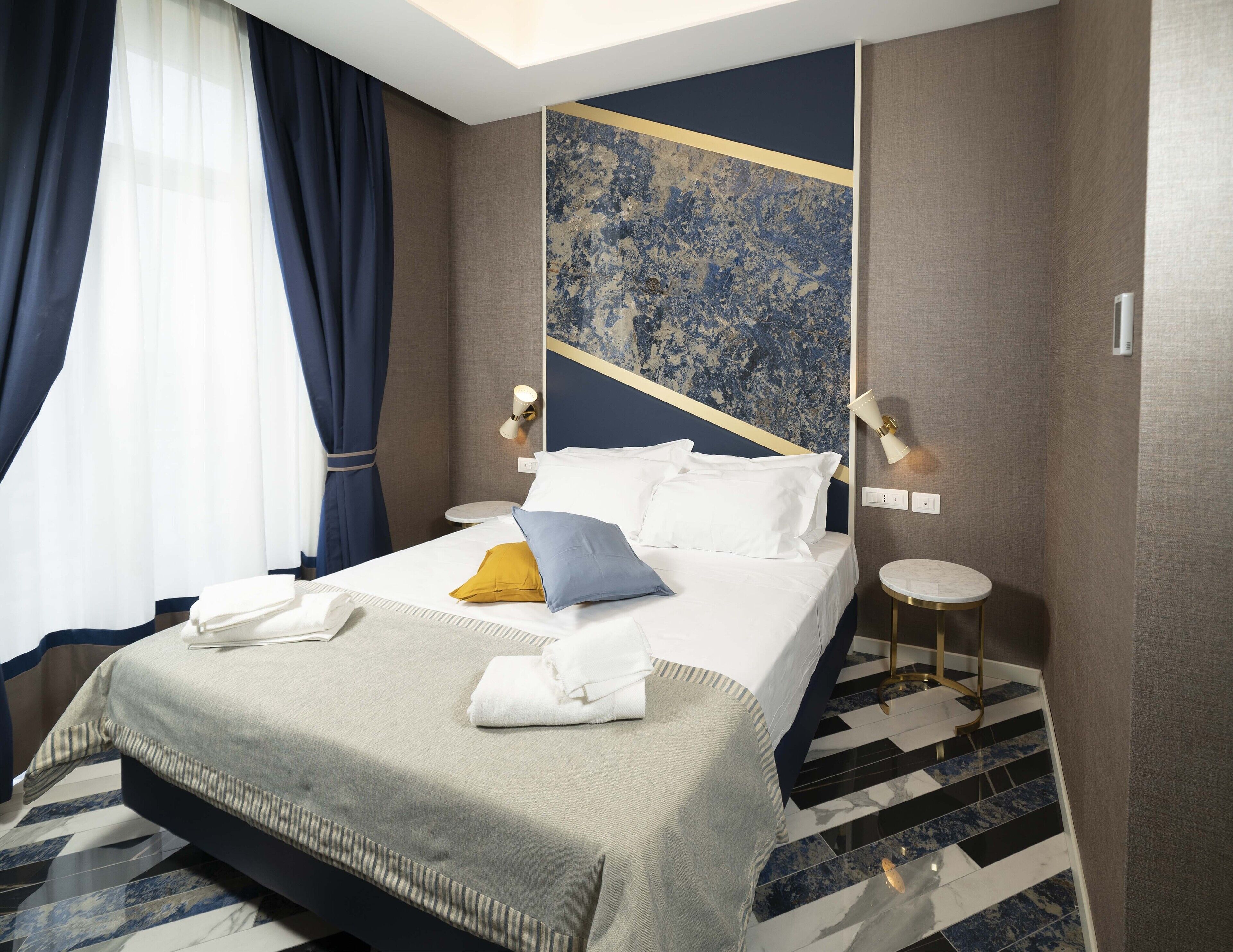 Una habitación de hotel con cama, mesitas de noche, una pared con diseño geométrico y suelo estampado.