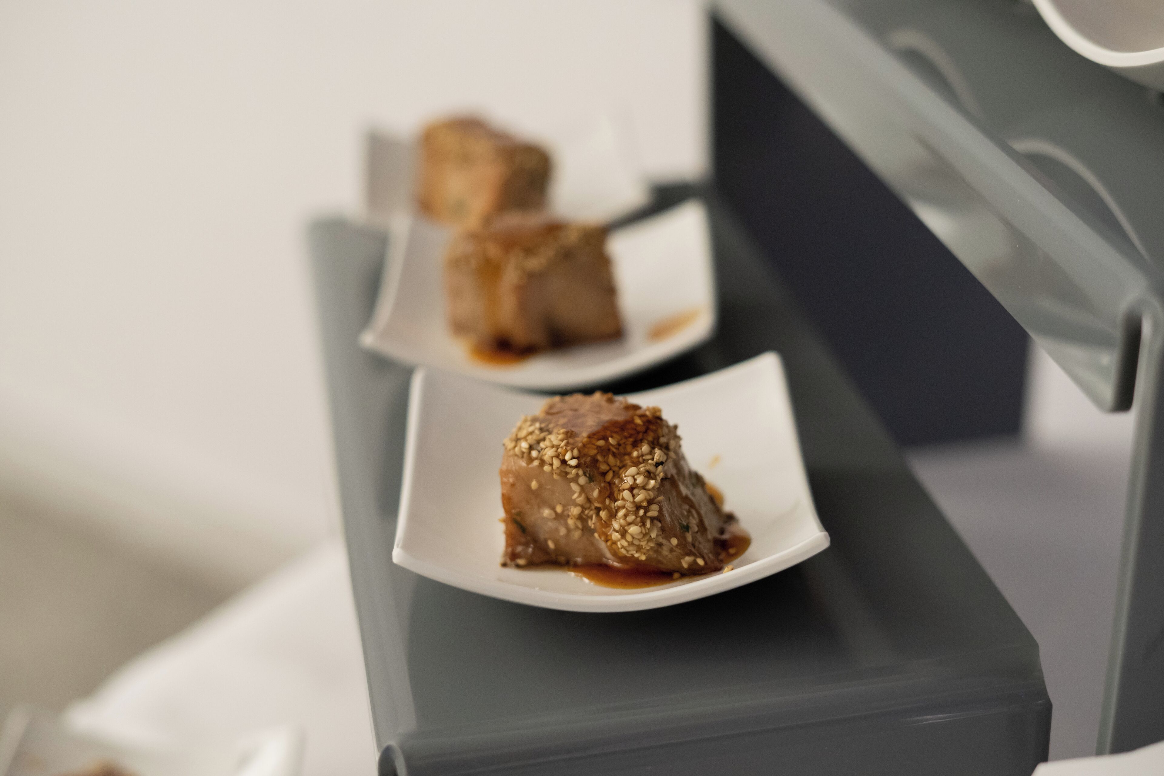 A dessert presentation on a white plate with sesame seeds, placed on a dark surface.