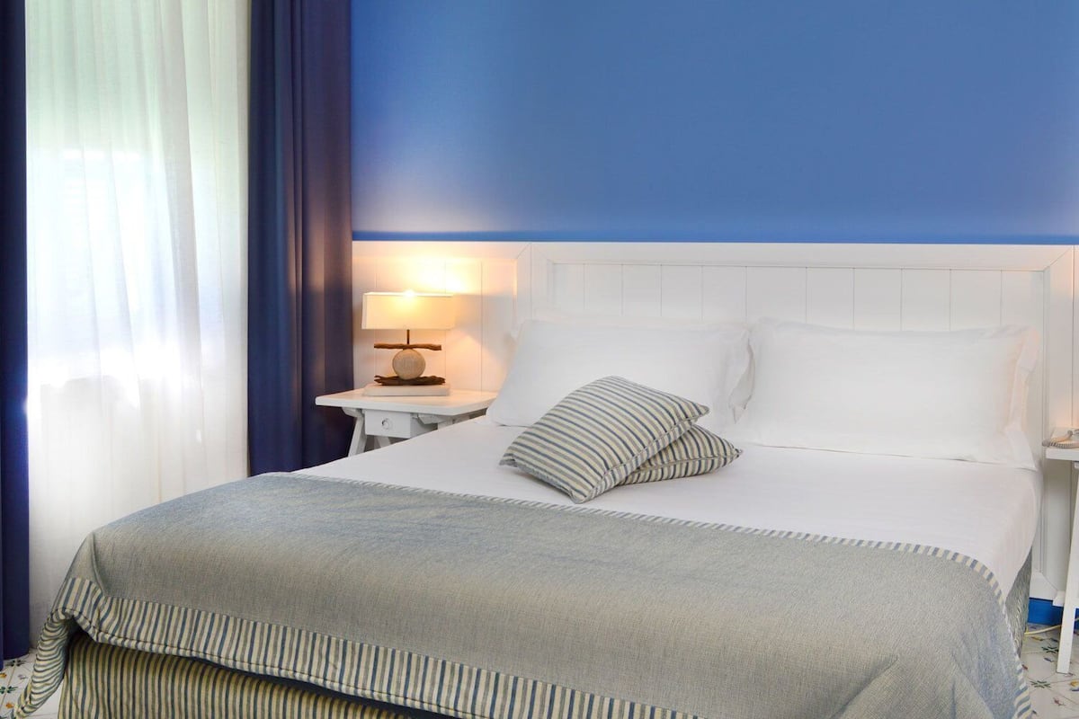 A hotel room with a bed, a nightstand with a lamp, and a window with curtains.