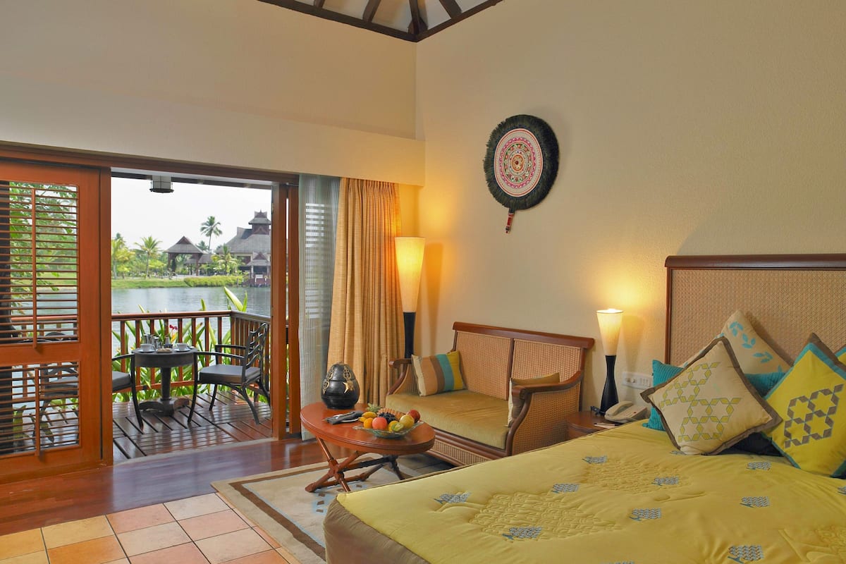 A hotel room with a bed, a table with chairs, a view of a water body, and a balcony.