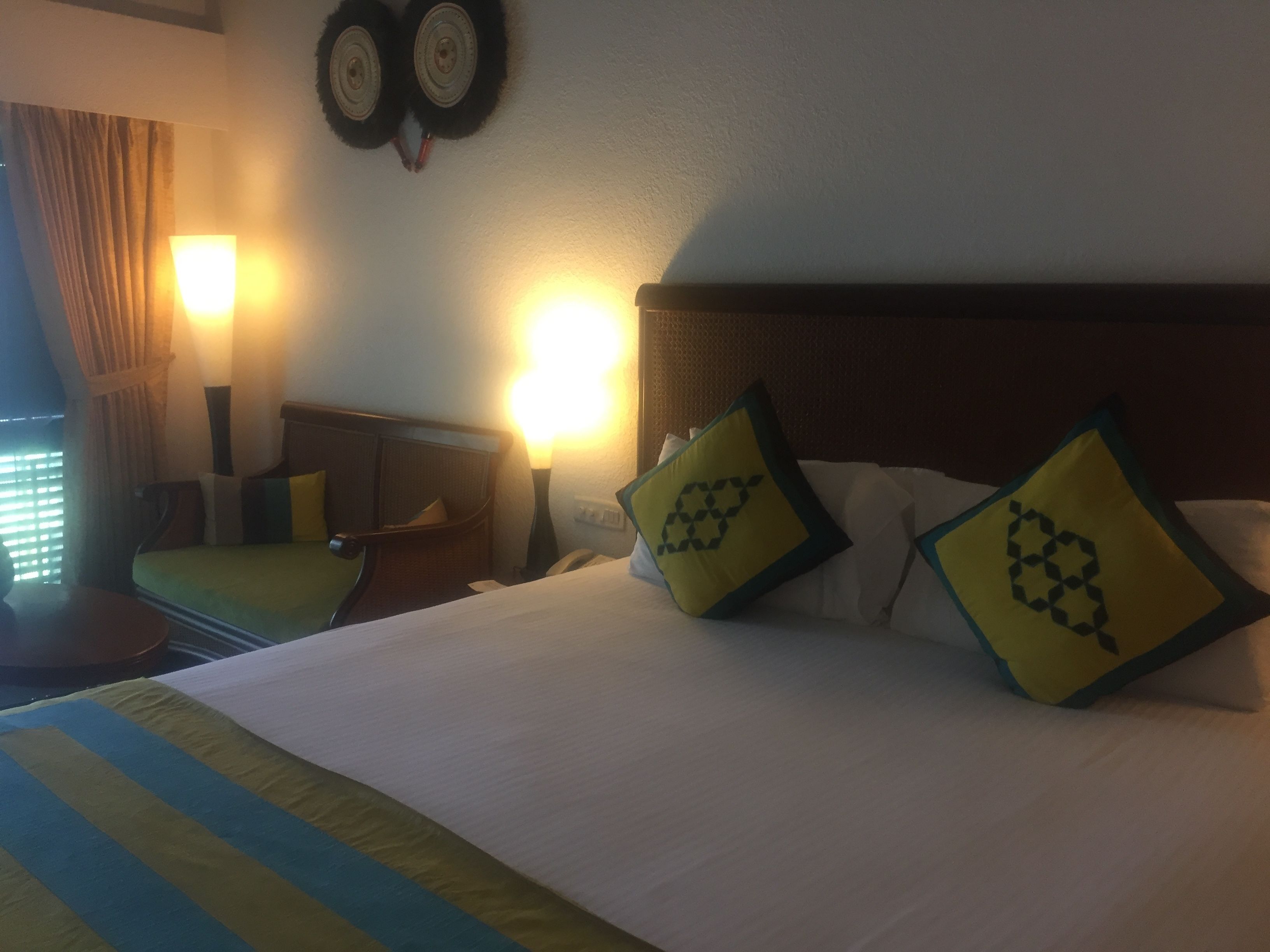 A hotel room with a bed, two bedside lamps, a nightstand, and a window with curtains.