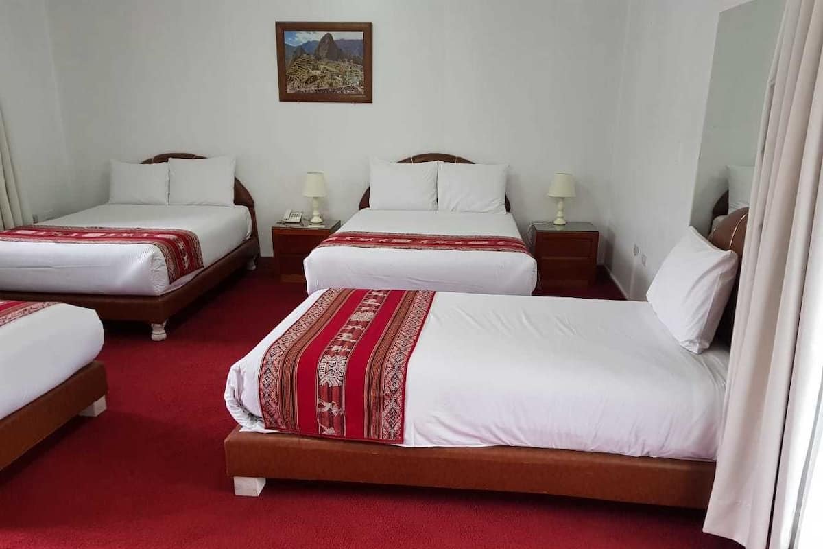 A hotel room with three beds, each with white bedding and red accents.