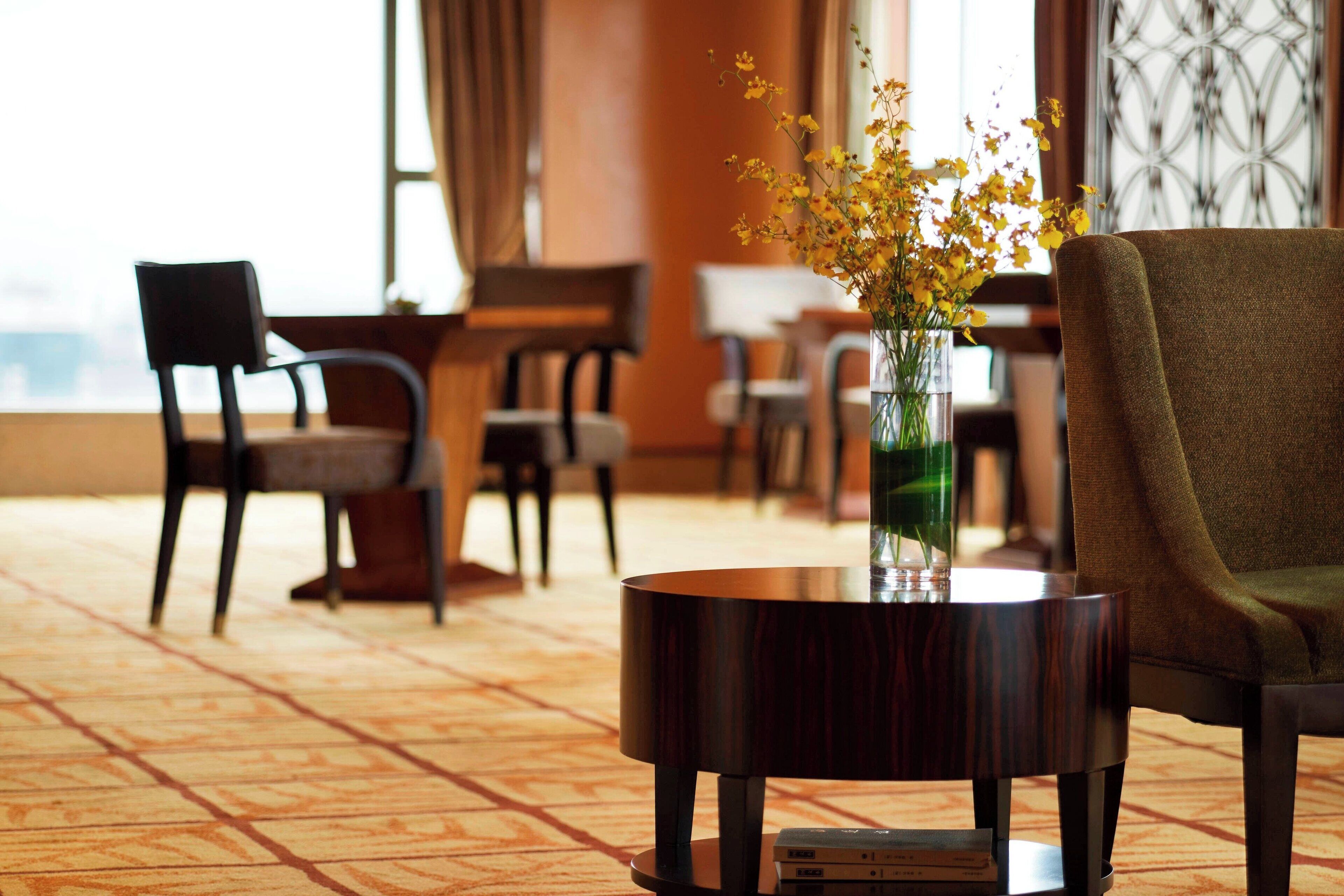 A room with a round wooden table, a vase with yellow flowers, and a green upholstered chair.