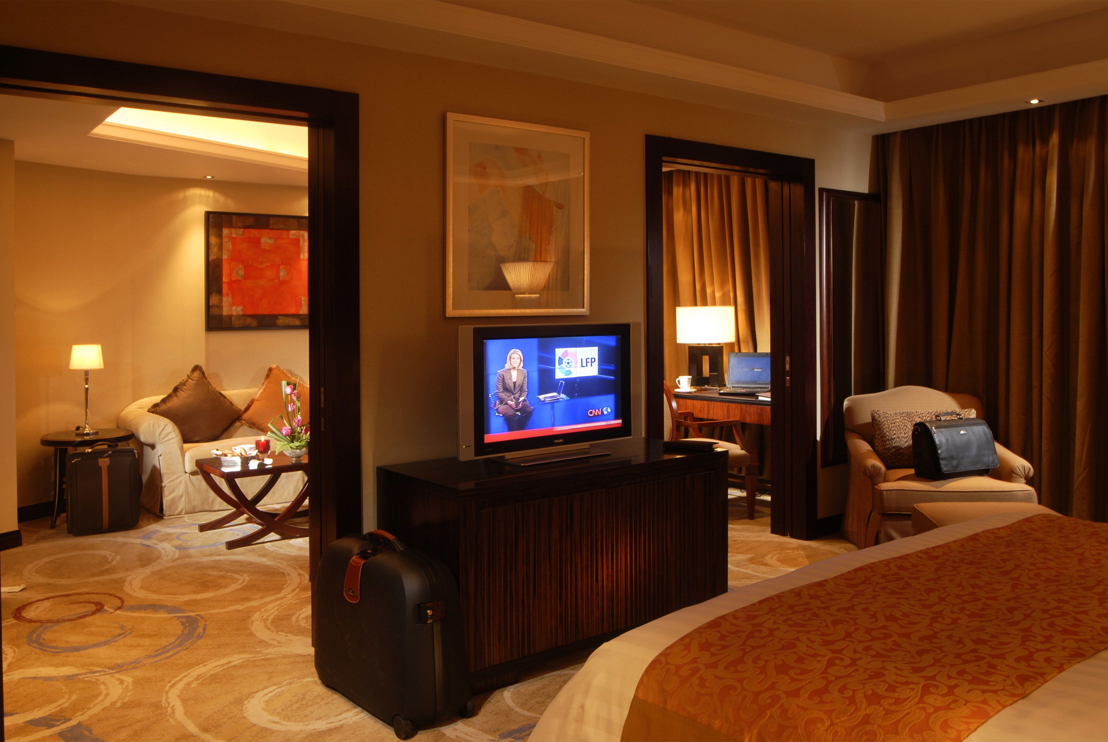 A hotel room with a bed, a desk, a television, a chair, and a suitcase.