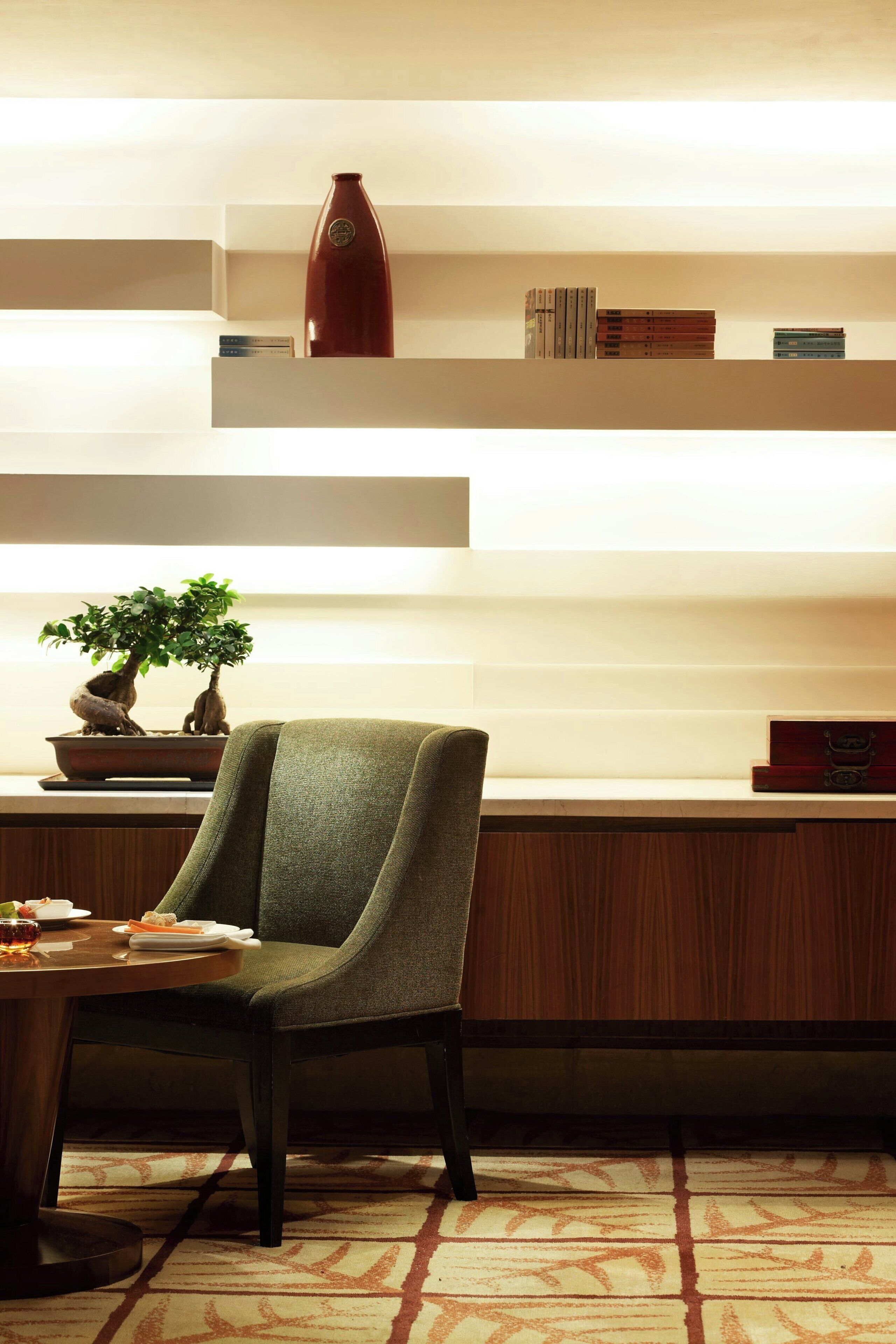 A modern interior with a green armchair, a bonsai tree, and a vase on a shelf.