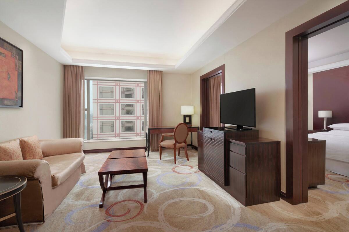 Quarto de hotel com sofá, escrivaninha, televisão e cama.