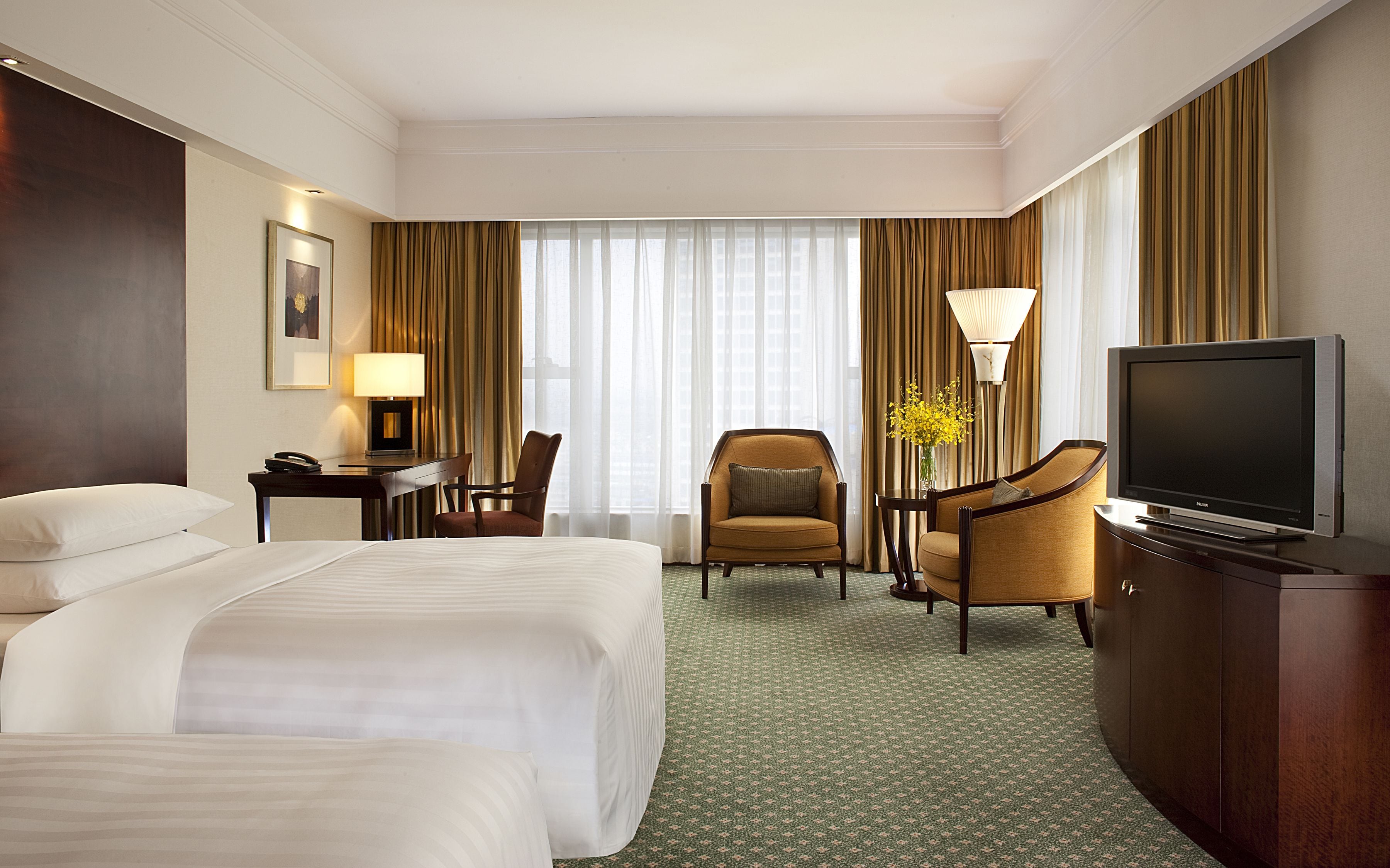 A hotel room with two beds, a desk with a lamp, a television, and a chair.