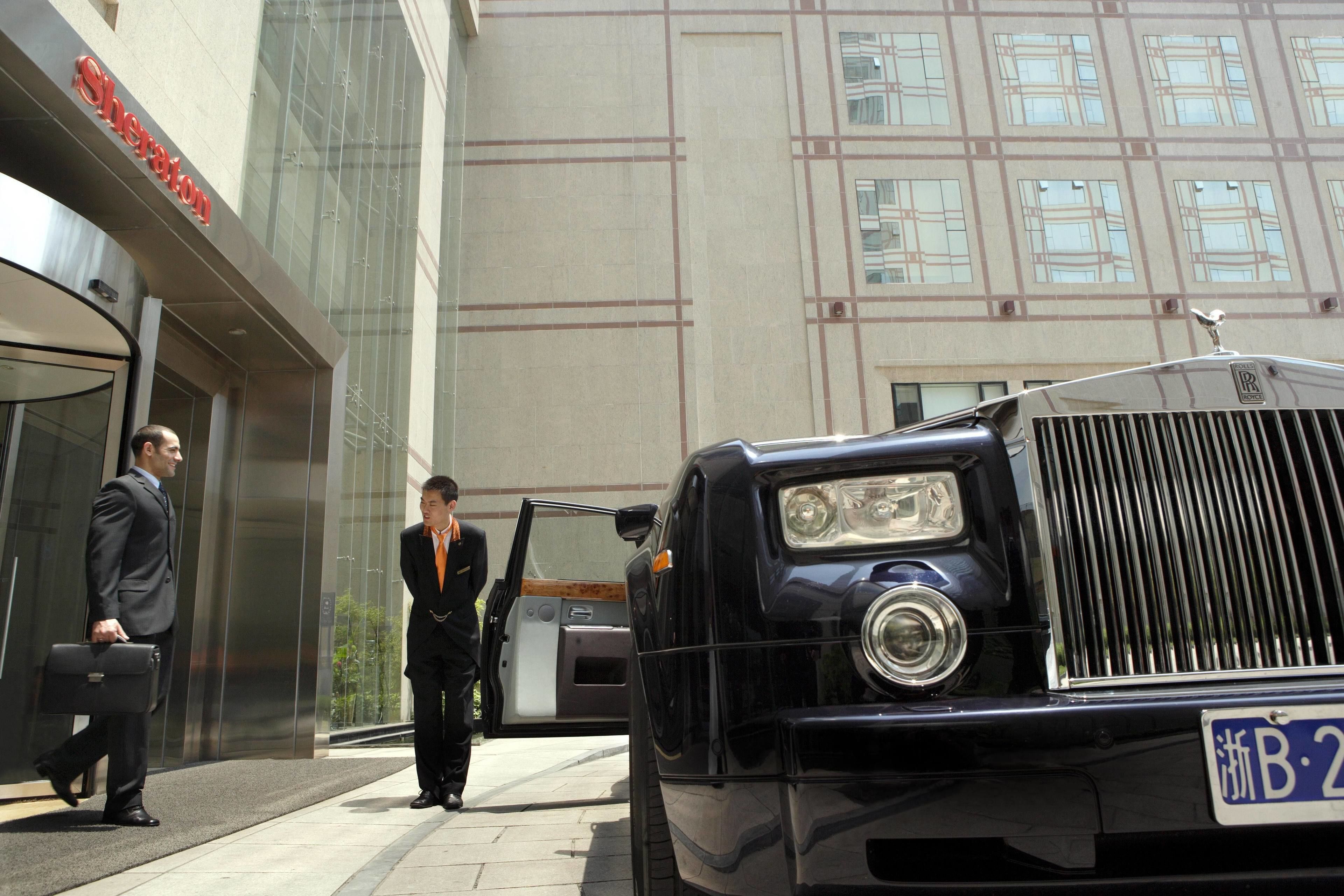 A black luxury car parked in front of a building with a sign reading "Sheraton."