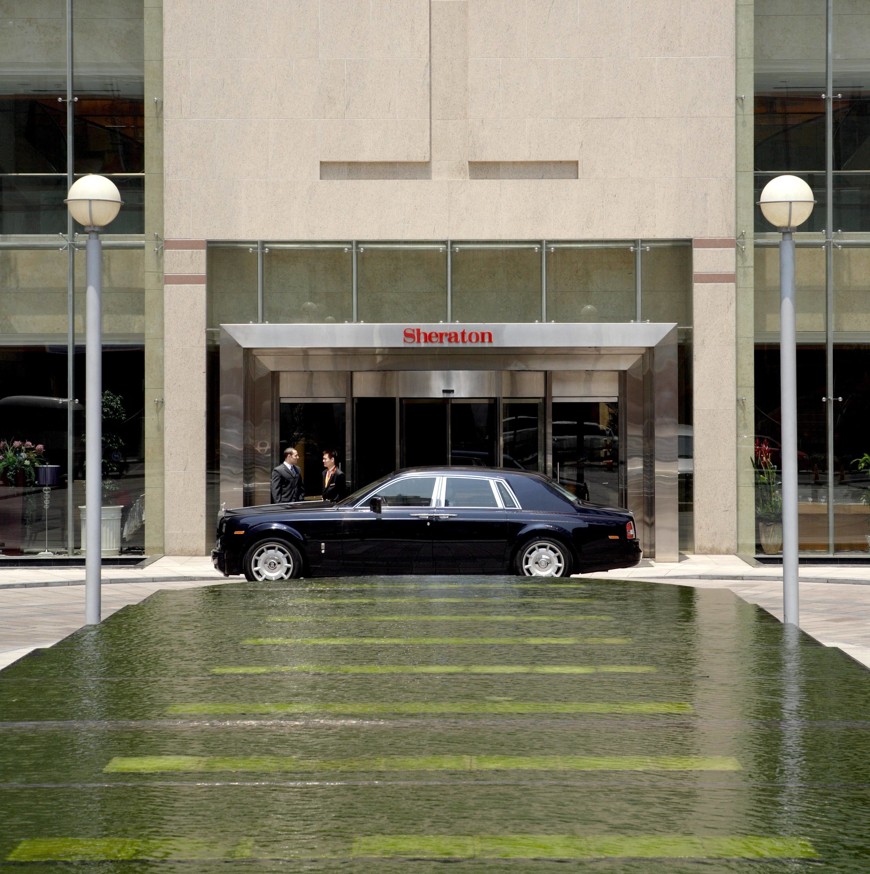A black car parked in front of a building with a 'Sheraton' sign.