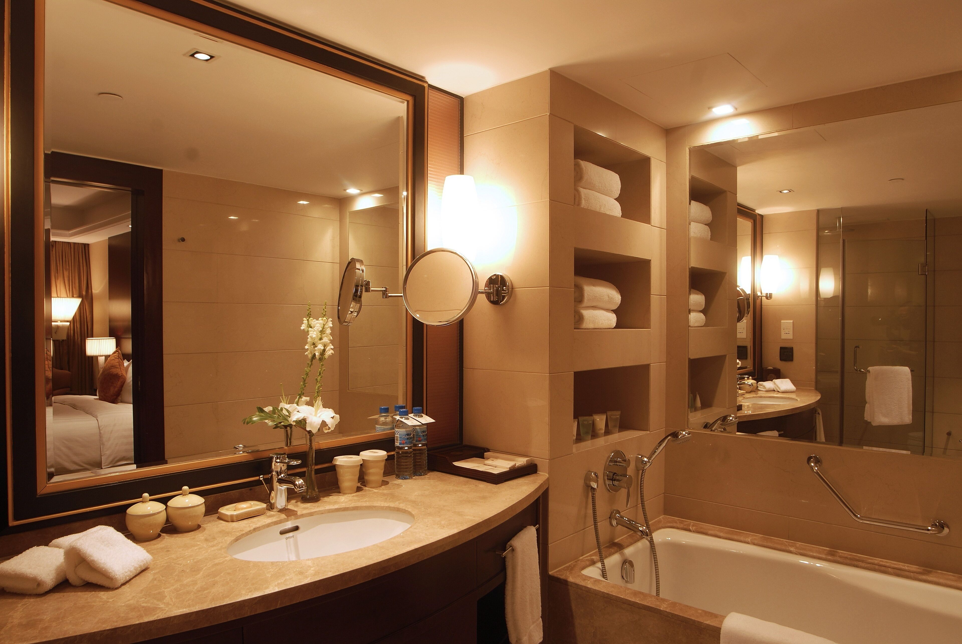 A modern bathroom with a large mirror, a bathtub, and a vanity with a sink and toiletries.