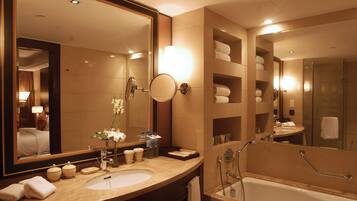 Un baño moderno con un espejo grande, una bañera y un tocador con lavabo y artículos de aseo.