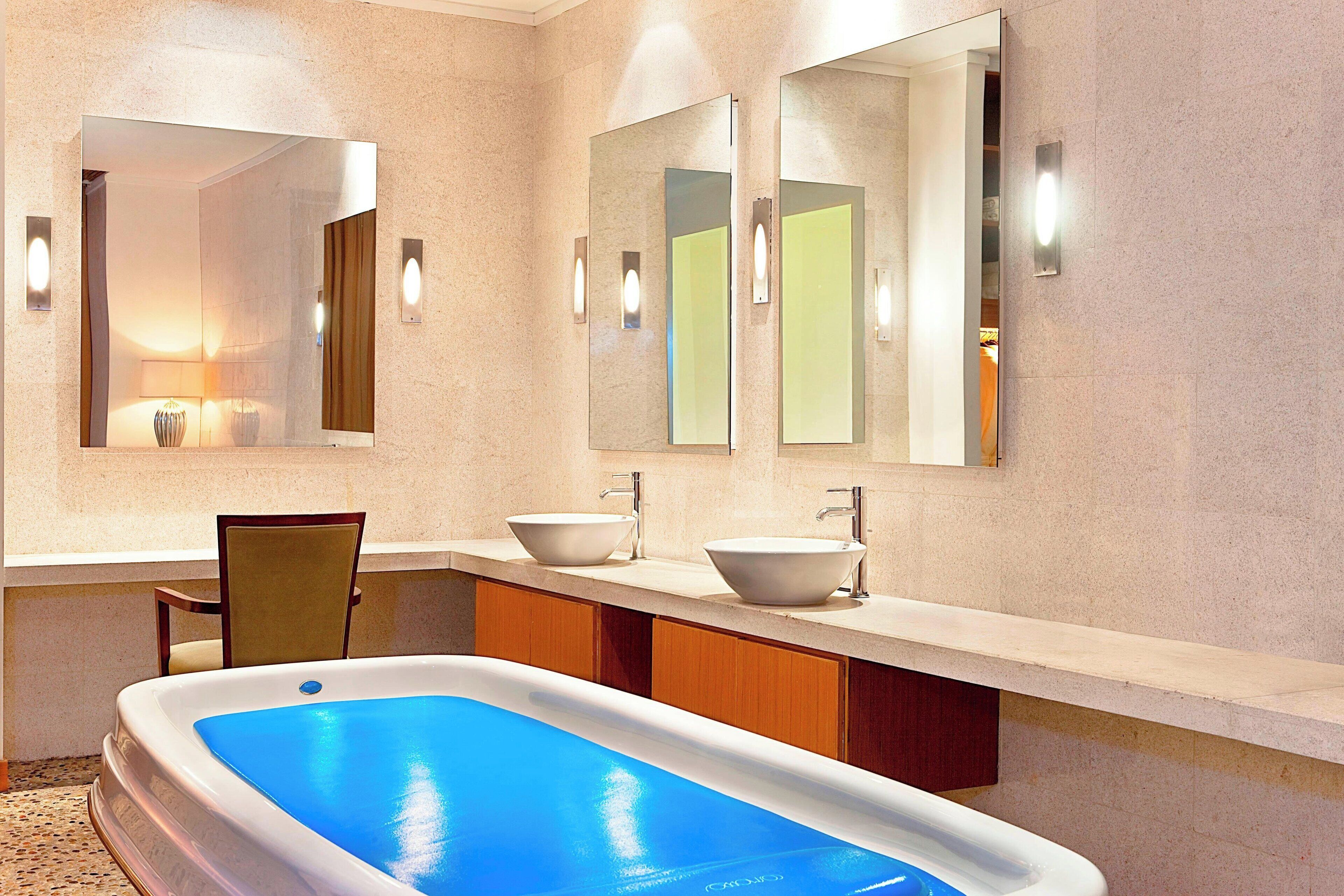A modern bathroom with a large bathtub, two sinks, and a chair.