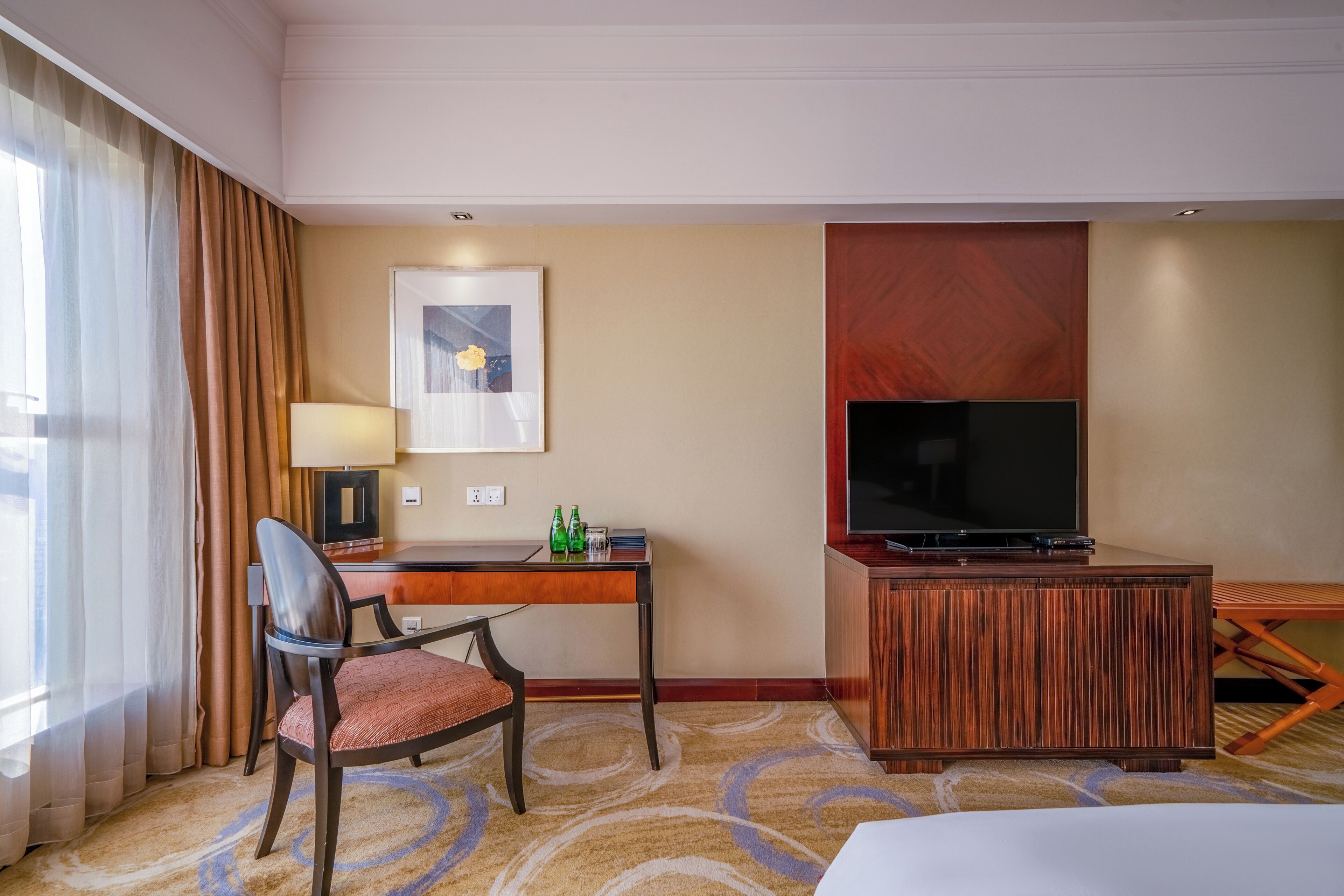 Habitación de hotel con cama, escritorio con silla, televisión, lámpara y un cuadro en la pared.