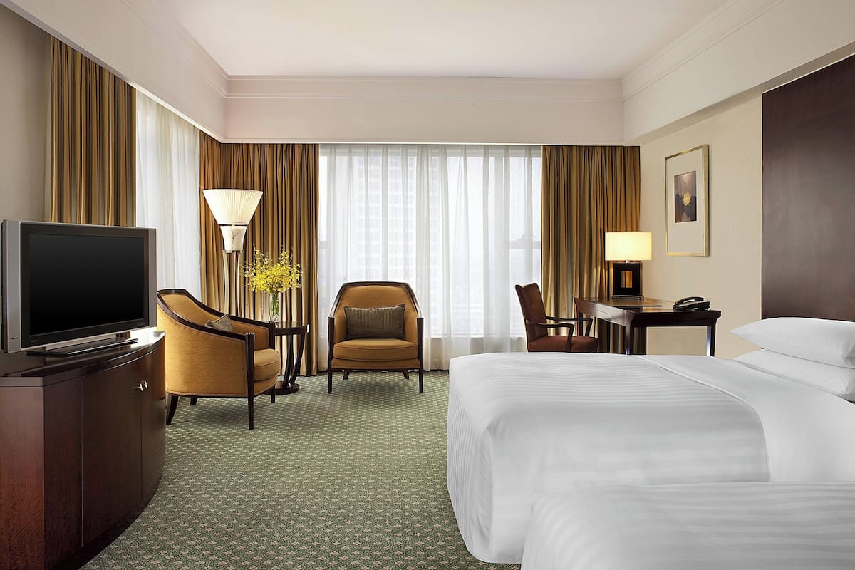 Quarto de hotel com uma cama grande, televisão, secretária com abajur e uma cadeira.