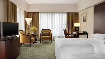 Una habitación de hotel con una cama grande, televisión, escritorio con lámpara y una silla.