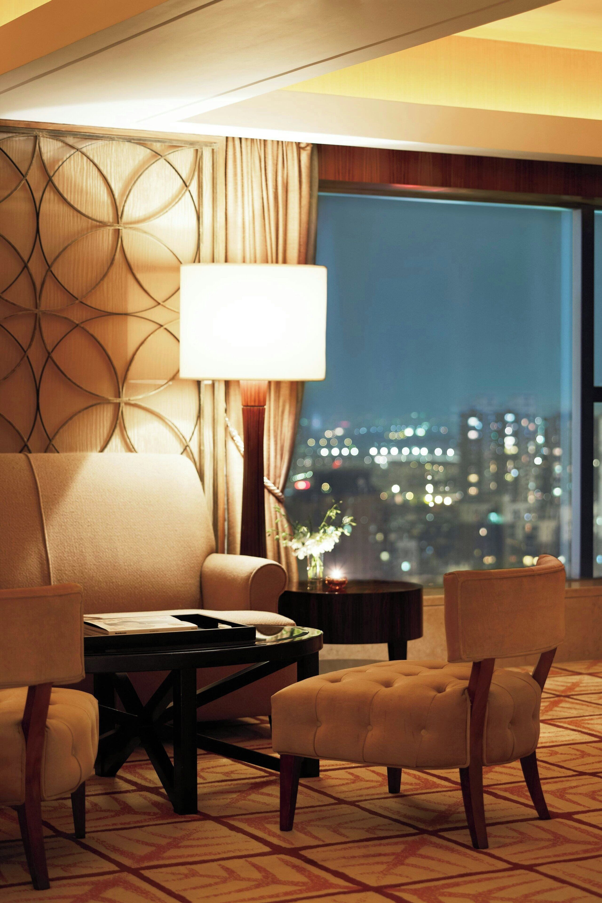 A hotel room with a large window, a sofa, two armchairs, a coffee table, and a lamp.