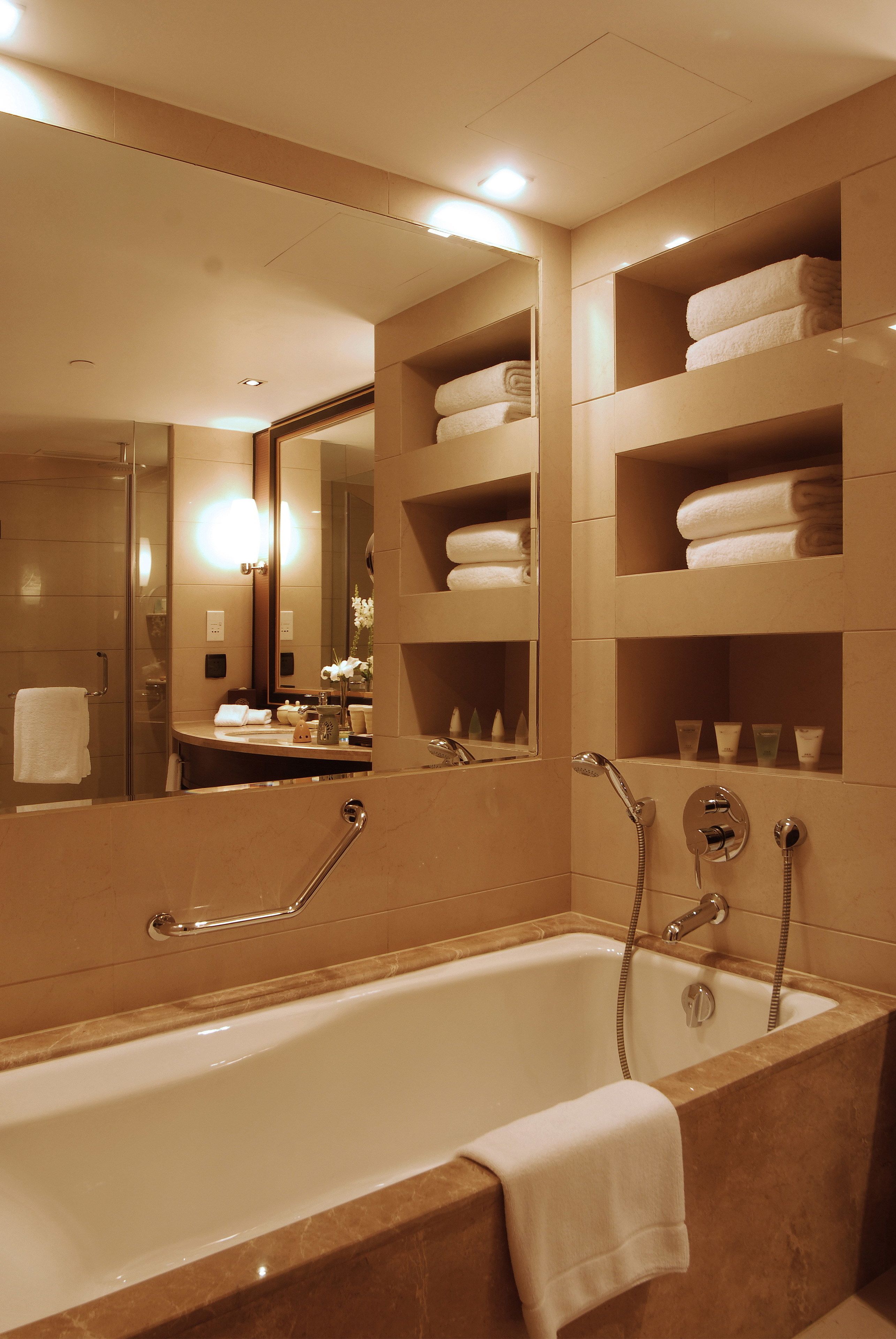 Ein modernes Badezimmer mit einer großen Badewanne, einer Duschkabine aus Glas und integrierten Ablagen mit Handtüchern.