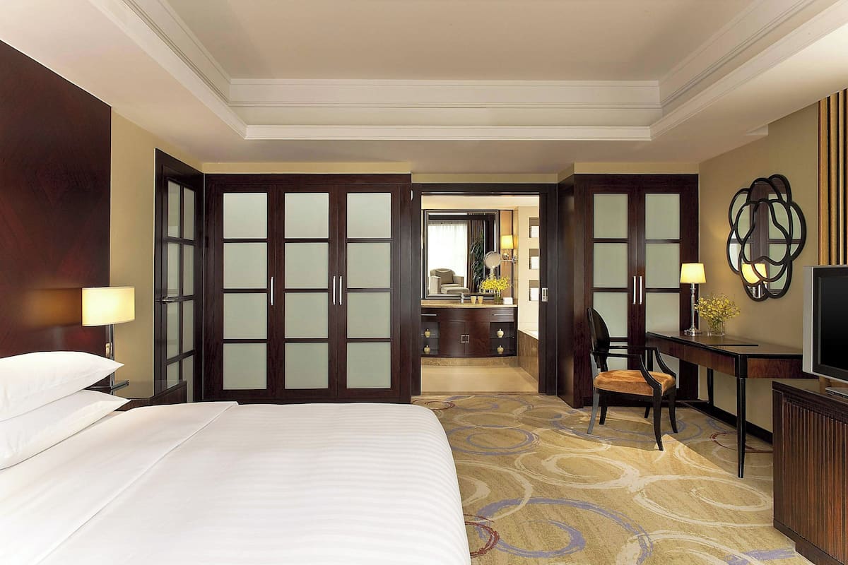 Quarto de hotel com cama grande, escrivaninha com cadeira, televisão e banheiro visível por uma porta aberta.