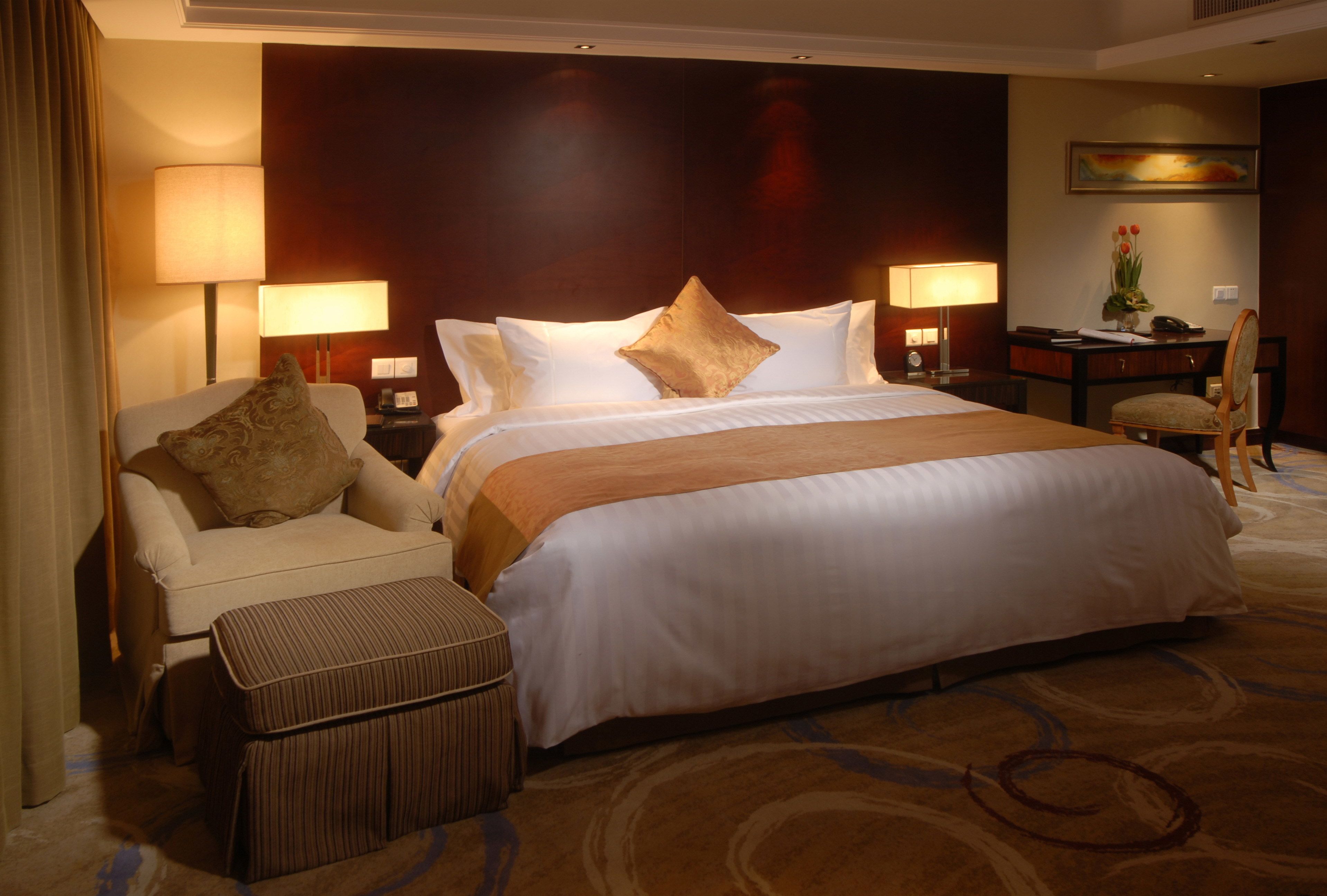 A hotel room with a large bed, two bedside lamps, a desk, a chair, and a small table with a vase of flowers.