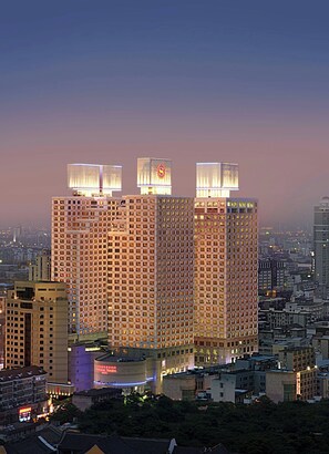 A high-rise hotel with a grid of windows, a prominent logo on the top, and a reflection in the water below. - Sheraton Ningbo Hotel (Ningbo)