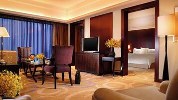 A hotel room with a television, a desk with a computer, a chair, a bed, and a large window with curtains.