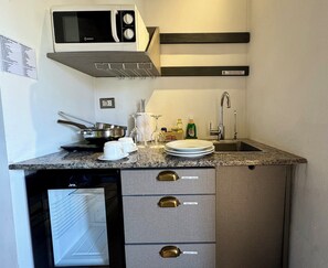 A compact kitchenette with a microwave, stove, sink, and storage drawers.