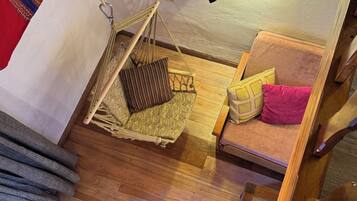 A cozy room with a hammock, a small sofa with cushions, and a wooden floor.